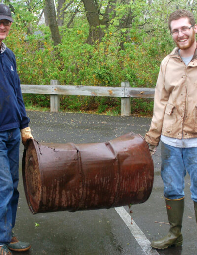 Two men removing steel drum from creek